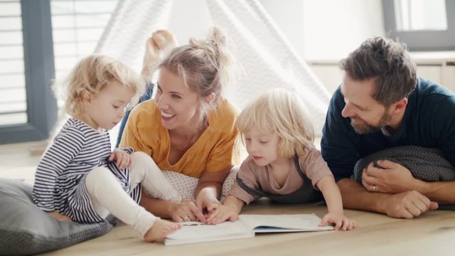 Young family with two small children indoors in bedroom reading a book.