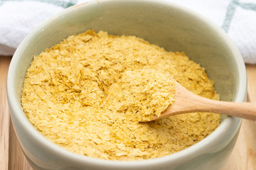 Beautiful top view closeup of Nutritional yeast in a ceramic bowl with wooden spoon, the yeast has yellow flakes, it's excellent source of vitamins, minerals, and high-quality protein. Vegan food.