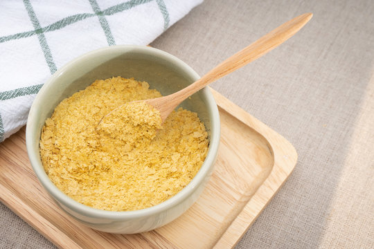 Top view & Closeup, Yellow flakes of nutritional yeast in ceramic bowl and wooden spoon, excellent source of vitamins, minerals, and high-quality protein for plant-based diet / vegan food.