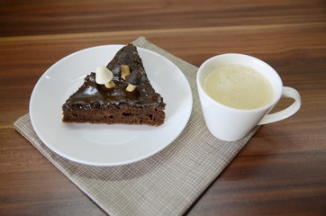Morning breakfast. On the table is a white ceramic cup with late, on a plate is a chocolate brownie dessert with mushrooms.