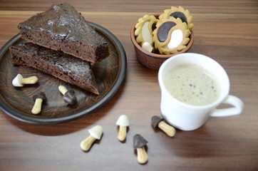 Morning breakfast. On the table is a white ceramic cup with late, on a plate is a chocolate brownie dessert, cookies.