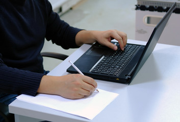 Engineer working on computer and taking some notes on a white paper