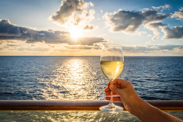 During sunset a female hand toasts the new year with a glass of white wine. Photo taken on a balcony of a cruise ship with a sea view.