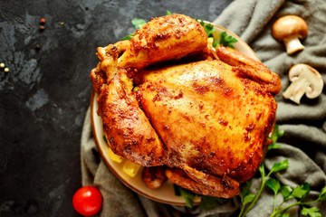 Whole baked chicken with lemon and mushrooms, on a dark background with textile. Curry chicken with a golden crisp.