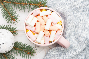 Hot chocolate with marshmallows in a pink mug on a white table wrapped in a warm sweater