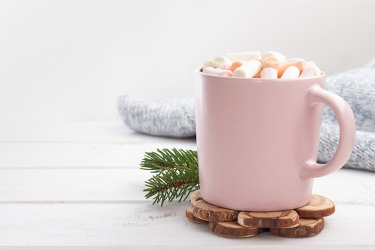 Hot chocolate (cocoa) with marshmallows in a pink cup on a white wooden background