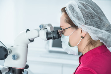 Close-up of a female dentist doctor looking in at a microscope in a dental office