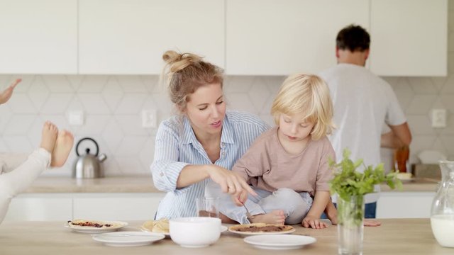 Young family with two small children indoors in kitchen, making pancakes.