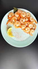 Cooked prawns are served on a plate with lemon and pepper.