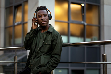 african-american man in stylish jacket in wireless headphones listening music on the street of the...