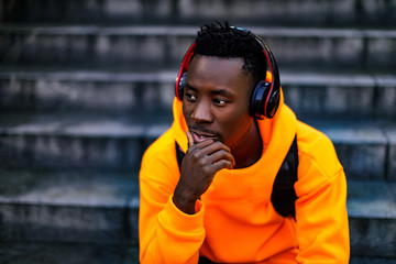 african-american man in stylish orange hoodie sweatshirt in wireless headphones listening music and...
