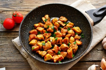 Chicken meat in a pan. Sliced ​​ chicken breast fried in a pan, wooden background.