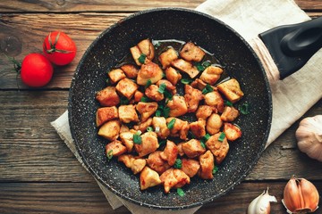 Chicken meat in a pan. Sliced ​​ chicken breast fried in a pan, wooden background.