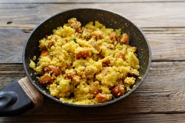 Couscous in a pan on a wooden background. Couscous with pieces of chicken in a pan.
