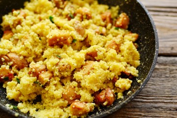 Couscous in a pan on a wooden background. Couscous with pieces of chicken in a pan.