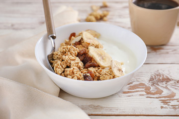 Tasty granola with yogurt in bowl on wooden table