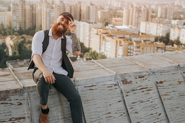 Cheerful stylish male adjusting cap on rooftop