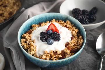 Tasty granola with yogurt in bowl on grey background