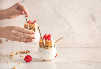 Female hands with glass of tasty granola and yogurt on white background