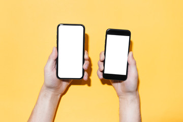 Close-up of male hands holding two different smartphones with mockup isolated on yellow background.