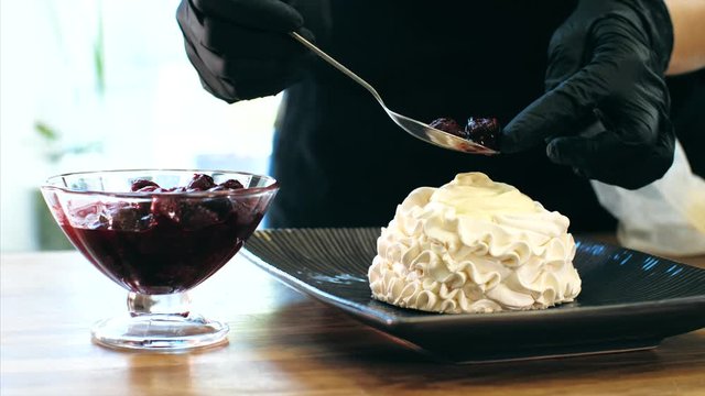 Chef cooking meringue cake, close-up. Cook puts a cherry jam on meringue while preparing sweet dessert.