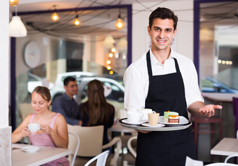 Fototapeta premium Portrait of glad waiter inviting to coffee