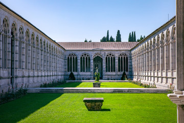 View from gallery on internal garden, Camposanto Monumentale di Pisa. Monumental Cemetery courtyard. Ornate columns and arches. Pisa, Italy, Tuscany