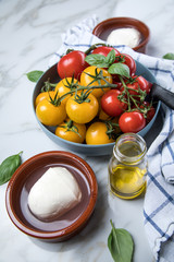 Rote und gelbe Tomaten mit Mozzarella, Basilikum und Olivenöl auf Marmor Hintergrund