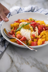 Frau isst Mozzarella Kugel mit roten und gelben Tomaten, Basilikum und Olivenöl auf Teller und ...