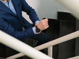 Man in blue blazer jacket walking upstairs while fixing his watch band