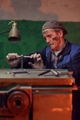 Serious senior man in work wear turning the lever while working at the lathe in the factory