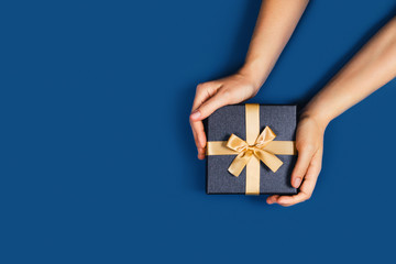 Gift box with surprise in a female hands on classic blue background. Flat lay, top view, place for...