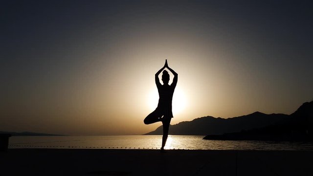 Silhouette of girl balancing in yoga asana at sunset by the sea