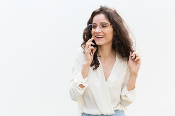 Happy joyful student girl in glasses speaking on cellphone, smiling, laughing. Wavy haired young woman in casual shirt standing isolated over white background. Nice phone talk concept
