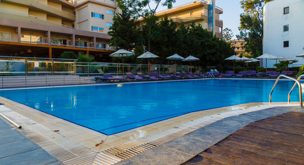 Beautiful tropical beach front hotel resort with swimming pool, sun-loungers and palm trees during warm sunny day, paradise destination for vacations