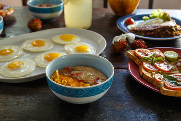 wooden table is covered with a healthy variety of natural food, banana porridge, scrambled eggs, omelet with vegetables, coconut, dragon eye.