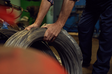 Close-up of manual worker holding metal cables while working in the factory