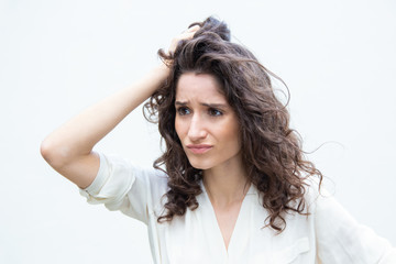 Stressed pensive desperate woman scratching head and looking away. Wavy haired young woman in casual shirt standing isolated over white background. Difficult decision concept