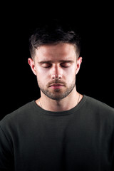 Fototapeta premium Studio Portrait Of Young Man With Serious Expression And Closed Eyes Against Black Background