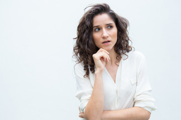 Fototapeta na wymiar Focused pensive female customer touching chin and staring away. Wavy haired young woman in casual shirt standing isolated over white background. Finding solution concept