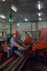 Serious mature engineer in protective eyeglasses and in work helmet controlling the machine in the factory