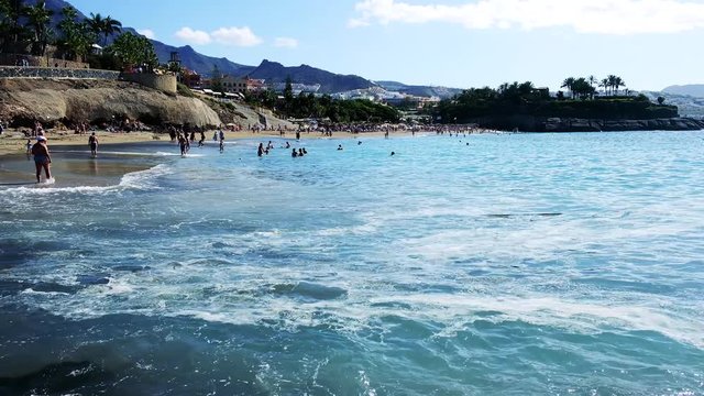 COSTA ADEJE, TENERIFE, SPAIN - NOVEMBER 2019: People lay on the sand and swim in the ocean at tropical beach.
