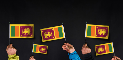 Fototapeta na wymiar Hands holds flags of Sri Lanka on dark background