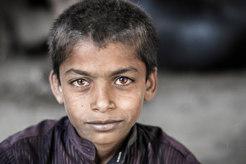 closeup of a poor staring hungry orphan boy in a refugee camp with sad expression on his face and...