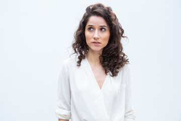 Pensive female customer looking up, studying copy space. Wavy haired young woman in casual shirt standing isolated over white background. Advertising concept