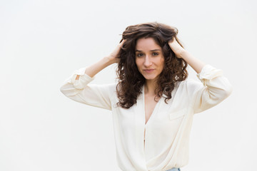 Naklejka premium Happy positive woman setting curly hair with fingers, massaging head skin. Wavy haired young woman in casual shirt standing isolated over white background. Beauty care concept