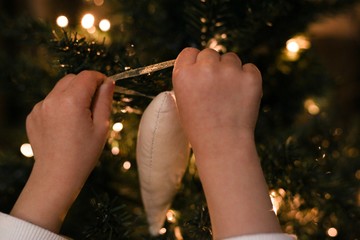 Baby decorating Christmas tree with soft toys. Kid’s hands hanging Christmas toy upon a tree - 308924576