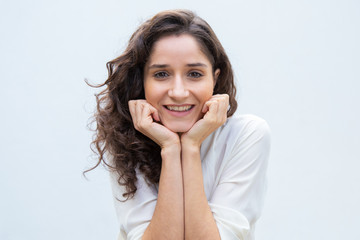 Happy beautiful student girl leaning chin and head on hands, smiling, looking at camera. Wavy haired young woman in casual shirt standing isolated over white background. Female portrait concept