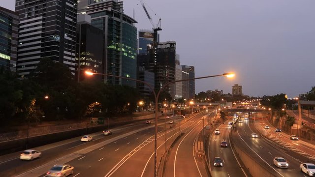 High-rise office towers in North Sydney standing above huge wide Warringah motorway toll road at sunset with driving motor traffic.