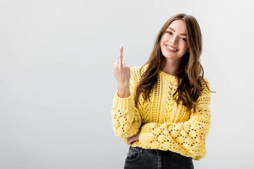 cheerful girl looking at camera while showing middle finger isolated on grey